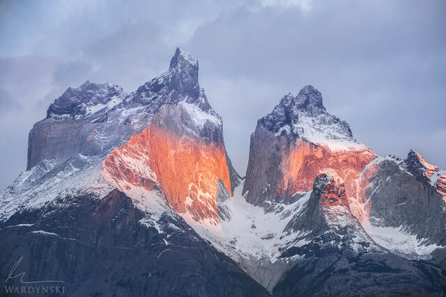 Fine art photograph of Cuernos Del Paine in Torres Del Paine. The rock is cloaked in the warm light of morning with cool blue clouds and shadows.